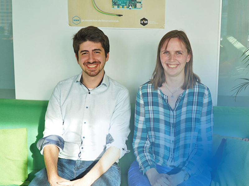Foto von Anwendungsentwicklerin Julia Lehmann (rechts) und Anwendungsentwickler Daniel Oberhammer (links) sitzend