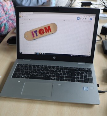 Laptop mit Skateboard-Entwurf © LHM Das Bild wurde über die Schulter eines Mädchens aufgenommen, das vor einem Laptop sitzt. Auf dem Bildschirm ist das Programm Tinkercad geöffnet, mit dem man Entwürfe für einen 3D-Druck entwerfen kann. In diesem Fall wurde ein Skateboard mit dem Schriftzug it@m entworfen.